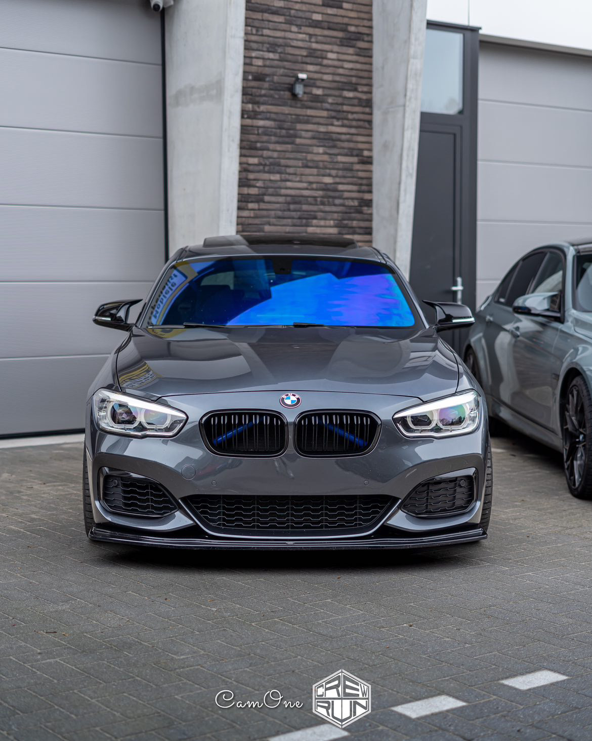 BMW M140i 2019 geparkeerd voor de garage van Crew Run in Mechelen waarvan de voorruit door High Tint is getint met Chameleon Tint
